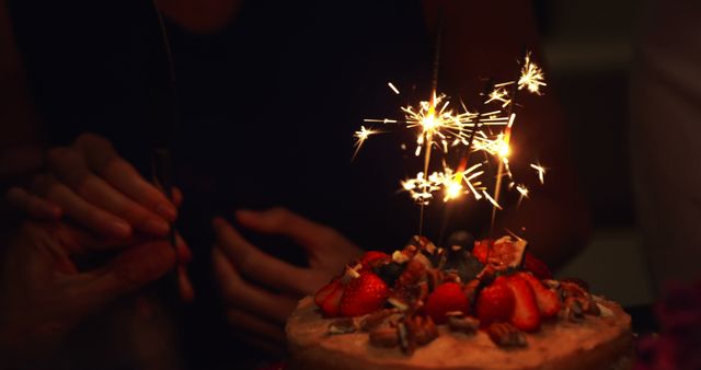 A birthday cake adorned with sparklers and fresh strawberries is presented by a person, creating a festive atmosphere. Celebratory moments like these evoke feelings of joy and are often shared among friends and family during special occasions.