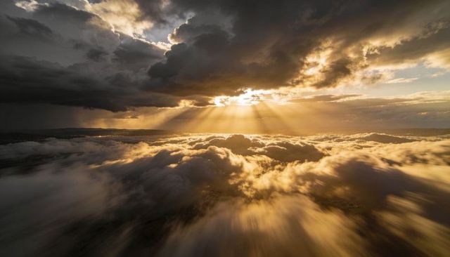 Golden Sunbeams Breaking Through Dark Storm Clouds Over Expansive Aerial Cloudscape