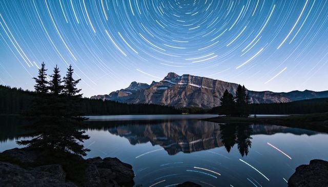 Star trails circling over mountain range reflecting in glassy alpine lake at night