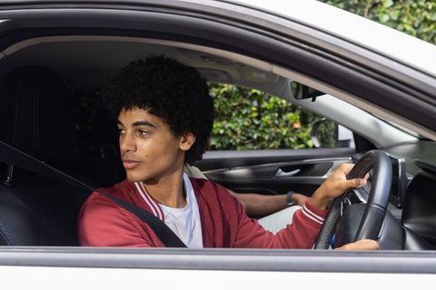 African american young man driving sedan looking left wearing seatbelt red jacket