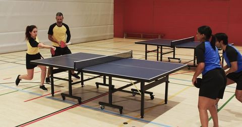 Doubles table tennis action in indoor gymnasium