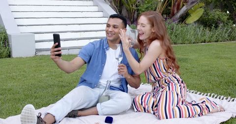 Engaged couple showing off ring in garden chatting on smartphone