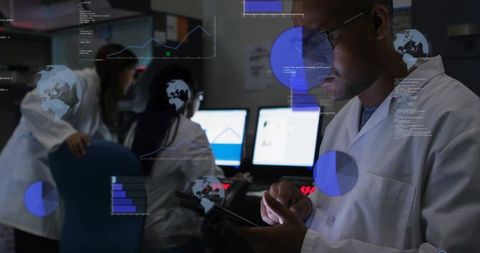 Male researcher monitoring tablet while colleagues analyze dashboards on dim laboratory monitors