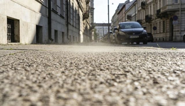 Low-angle pavement close-up revealing rough asphalt texture on urban street with parked cars