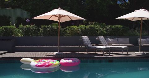 Colorful inflatable pool floats floating on turquoise backyard pool with sun loungers