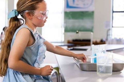 Young girl conducting hands-on science experiment with test tubes in bright classroom