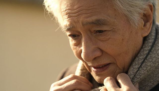 Elderly asian man holding scarf in warm sunlight closeup contemplative portrait