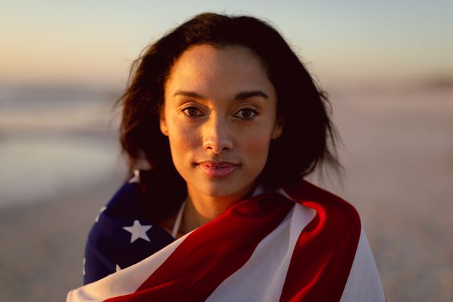 This image depicts a woman wrapped in an American flag standing on a beach at sunset. It can be used for themes related to patriotism, national pride, freedom, and independence. Ideal for use in advertisements, social media posts, and articles celebrating American holidays or promoting travel and tourism in the USA.