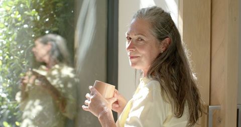 Mature Woman with Cup Contemplating by Sunlit Window