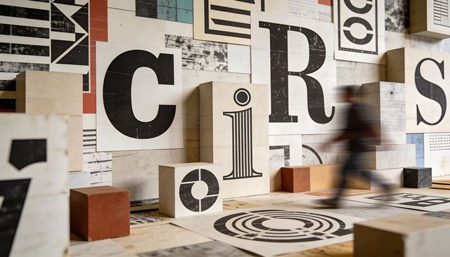 Oversized typographic installation with letter blocks, geometric floor graphics, motion blur