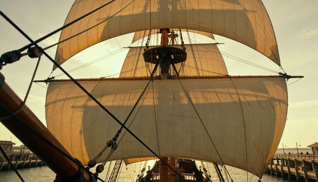 Golden backlit sails of historic tall ship filling harbor with rigging and crew activity