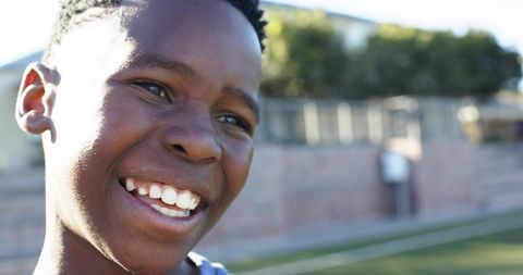 Joyful african teen smiling on sports field closeup portrait sunlit urban background