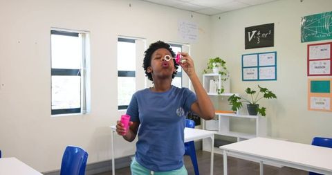 African girl blowing soap bubbles in bright classroom exploring creativity and science