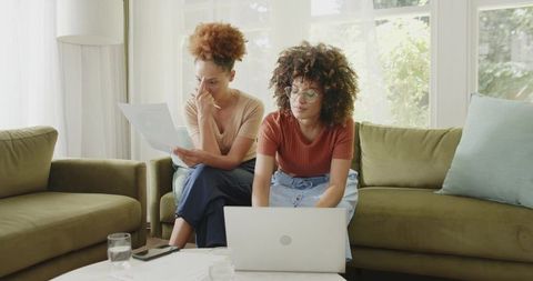African American Women Collaborating on Finances and Remote Work with Laptop on Sofa Now