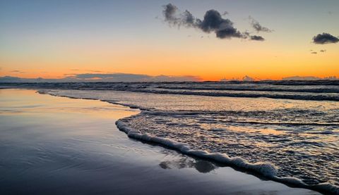 Tranquil ocean shore at sunrise reflecting soft hues in beach water