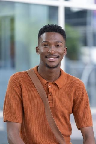 Smiling african man standing by glass facade wearing rust-orange polo and shoulder strap