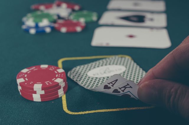 Person holding a winning poker hand with aces while betting chips are stacked on a green table. Useful for content related to casinos, gambling, luck, and entertainment. Great for illustrating tense moments in poker games or showcasing high-stakes gambling scenes.