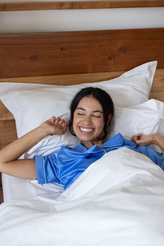 Smiling woman stretching in bed wearing blue satin pajamas cozy morning relaxation