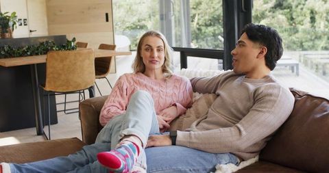 Couple relaxing on leather sofa in sunlit modern open-plan living room with glass doors
