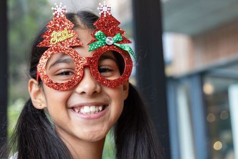 Indian girl smiling wearing red glitter christmas-tree novelty glasses at cafe window bokeh