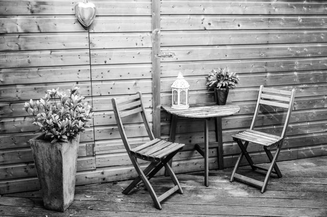 Patio portraying a cozy outdoor area with two wooden chairs and a matching table. Decorated with potted flowers and a stylish lantern. Ideal for articles on outdoor design, gardening tips, backyard makeover ideas, or rustic decor inspirations.