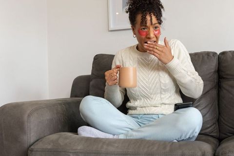 African american woman relaxing on sofa with under-eye gel patches and coffee mug