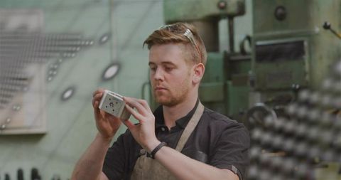 Machinist inspecting precision milled part on workbench wearing apron and safety goggles