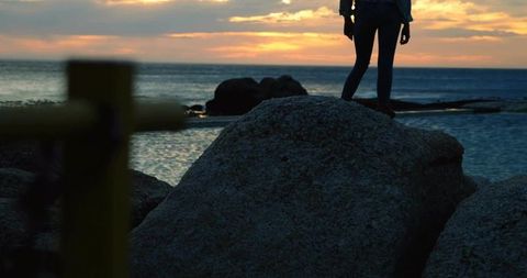 Woman Standing on Boulder Overlooking Ocean Sunset