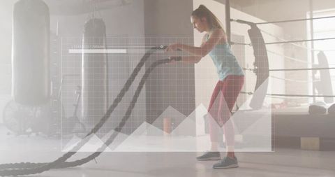 Woman swinging battle ropes with data overlay in boxing gym for strength and endurance