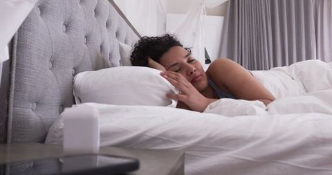 African american woman sleeping peacefully on white bed with tufted headboard and canopy