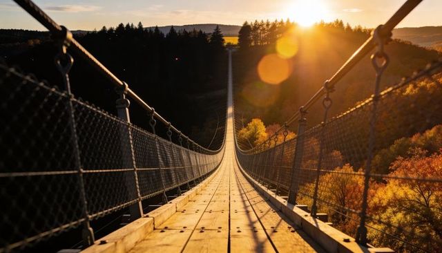 Sunlit suspension bridge leading across autumn valley at golden hour with warm lens flare