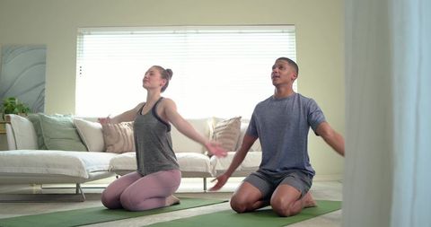 Young couple practicing morning yoga at home kneeling stretching and deep breathing
