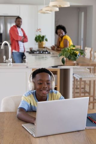 African american family watching child learning on laptop with headphones in kitchen