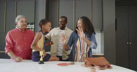 Multigenerational diverse family celebrating child victory with gold trophy in kitchen