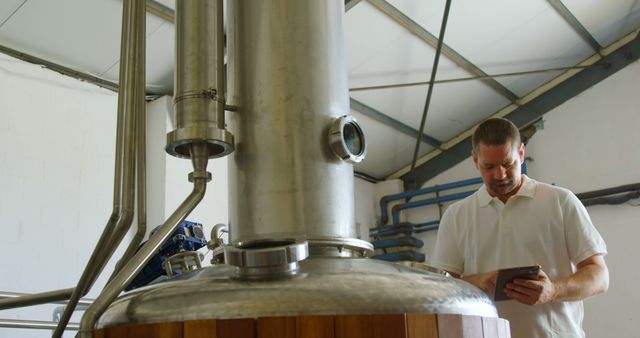 Brewery worker monitoring advanced stainless steel brewing equipment. Suitable for articles about industrial brewing, beer production, technology in fermentation, and professional work environments. Useful for illustrating modern brewing techniques and workplace environments in the alcoholic beverages industry.