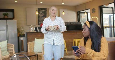 Friendly cafe server delivering two takeaway coffees to customer using smartphone, smiling