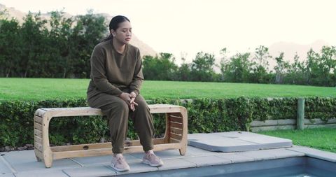 Woman in thought relaxing by poolside in tranquil backyard environment