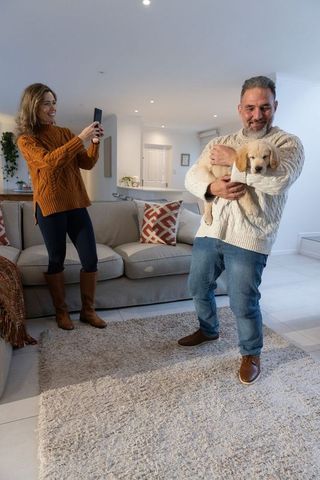 Couple cuddling puppy while partner taking smartphone photo in cozy modern living room