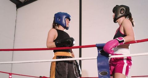 Female boxers sparring in ring corner exchanging glove taps during intense gym training