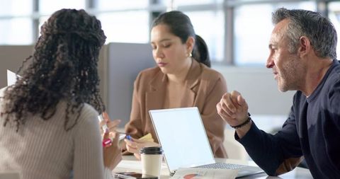 Diverse team collaborating over charts and laptop in modern open-plan office meeting