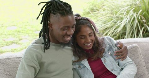 African American Man and Indian Woman Sitting on Outdoor Sofa Casually Smiling and Embracing