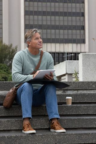 Middle-aged man sketching on urban steps with coffee and folio