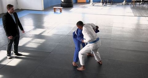 Coach Present as Trainees Grapple on Martial Arts Mats in Dojo