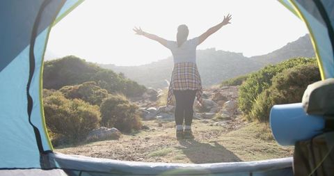 Woman embracing sunrise outside tent in mountain landscape