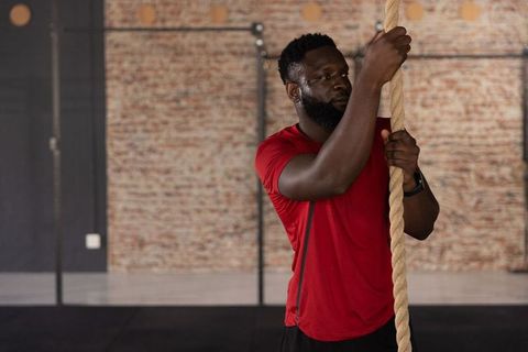 African american man gripping rope preparing for climb in industrial brick gym