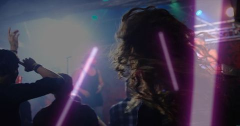 Long curly hair dancer moving through purple club lights with crowd and stage microphone