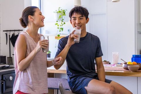 Young couple drinking smoothies and laughing in modern minimalist kitchen in activewear