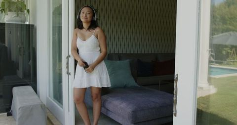 Smiling woman in white dress enjoying sunlight by open patio door