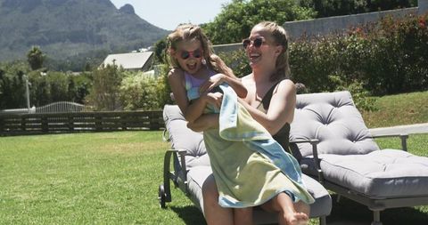 Mother wrapping daughter in towel on lounger in sunny backyard with mountain view