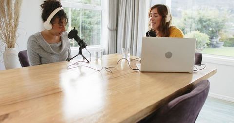 Recording home podcast together: two women podcasting with laptop, microphones, headphones